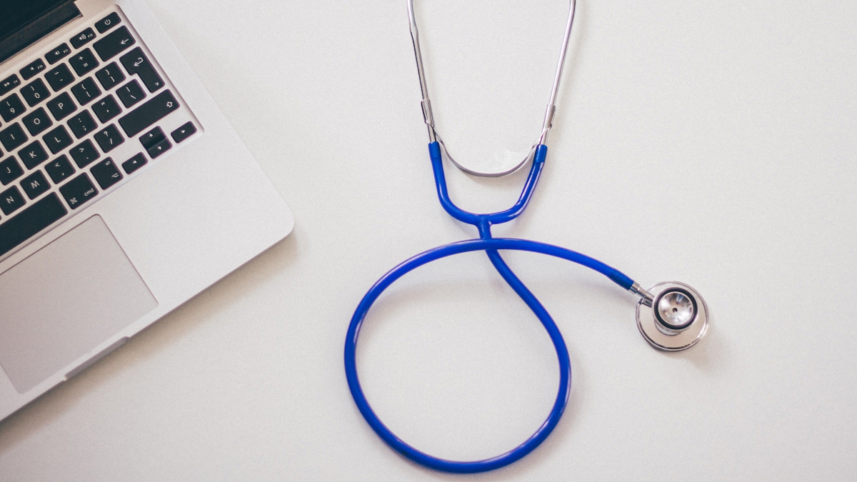 A blue stethoscope next to a macbook laptop on a white background